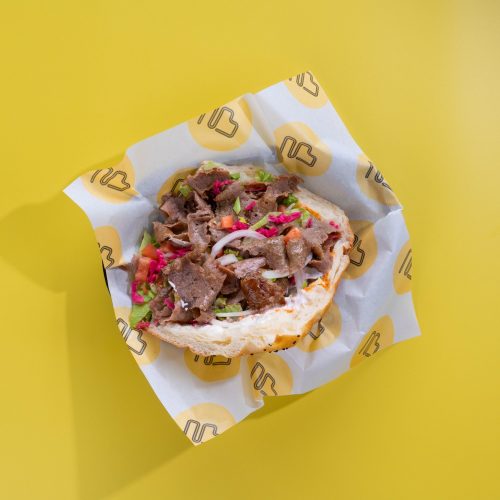 A close-up of a New Berlin Eats Döner Kebab served in a toasted, house-made turkish bread pocket with lamb, pickled red cabbage, and signature sauces.